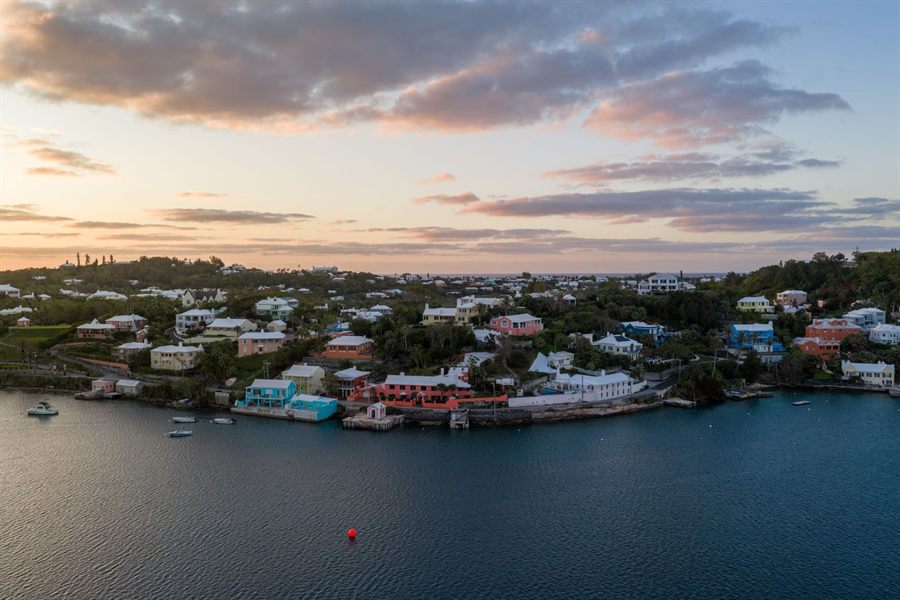 Aerial view of the Bermuda coastline at sunrise with pastel houses above calm water