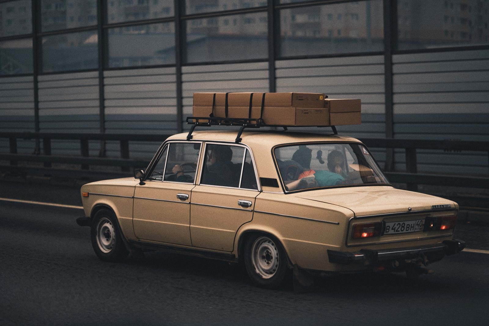Vintage car with boxes strapped to its roof driving along a city highway
