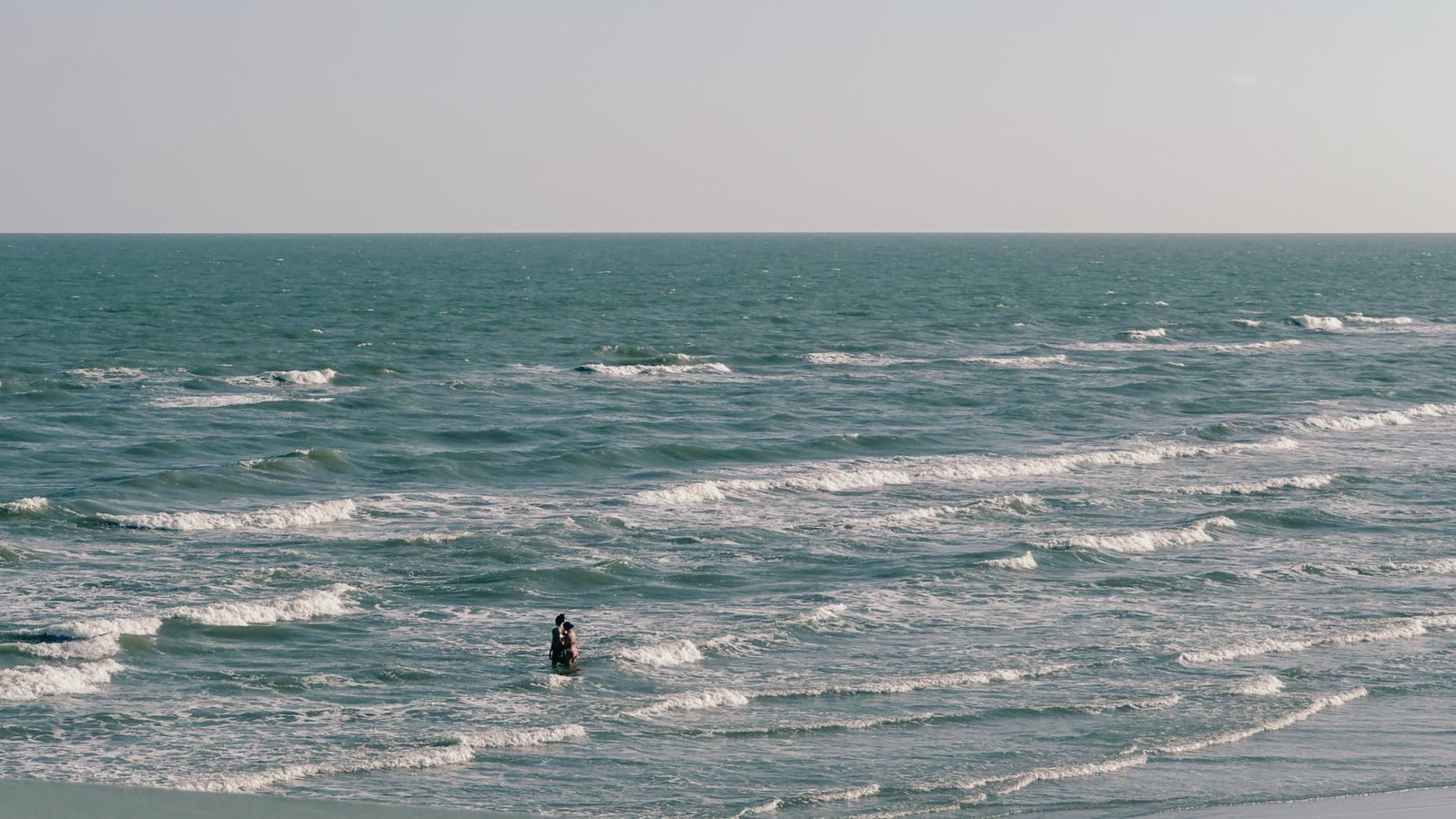 Waves rolling in on a Galveston beach in Texas with a lone swimmer offshore